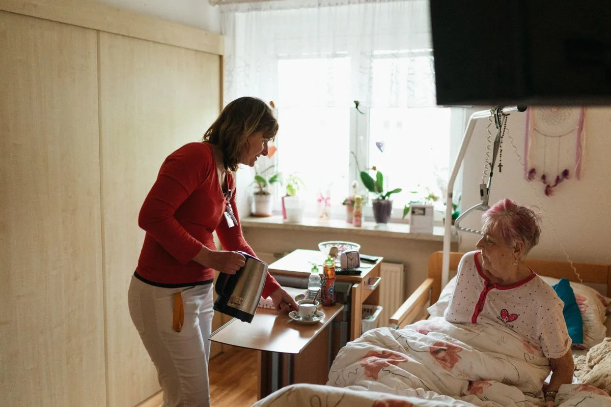 Pflegekraft versorgt eine ältere Frau in deren eigenem Schlafzimmer